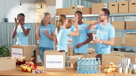 grupo multiétnico de voluntarios parados en un almacén de caridad aplaudiendo y dando cinco en un almacén de caridad