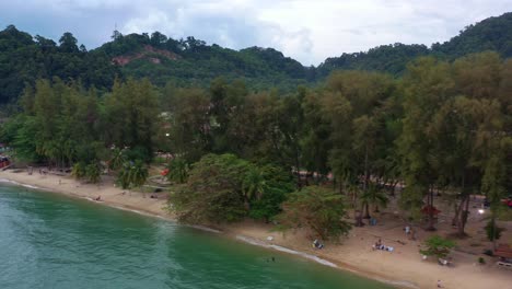 cinematic low level aerial drone fly along coastal shore of touristic destination teluk batik beach surrounded by lush green trees in a tropical atmosphere at lumut, perak, malaysia, southeast asia