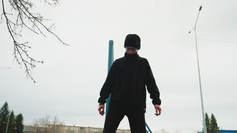 a young boy dressed in a black outfit and glasses carefully walks on an elevated structure, while another boy in a gray sweater hangs on an iron pole in the background