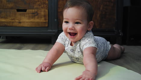 baby boy smiling on the ground while on his stomach learning how to crawl