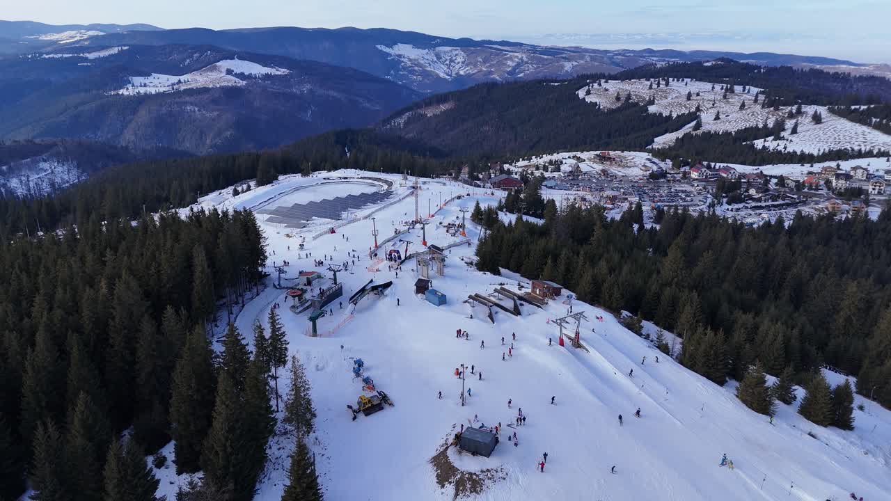 Letecký pohled z dronu na zasněženou sjezdovku v horách s lyžaři a snowboardisty za slunečného zimního dne. Koncept zimních sportů, turismu a venkovní rekreace.
