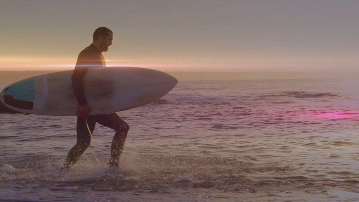 Surfboard entering from left causing mid-adult man running into shallow surf, surfing sunset waves