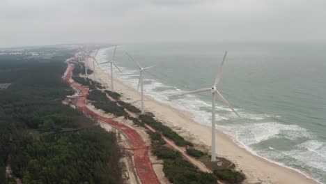 Eine-Reihe-Von-Onshore-Windturbinen-Mit-Horizontaler-Achse,-Die-Sich-An-Einem-Langen-Strand-Mit-Hoher-Meeresdünung-An-Einem-Bewölkten-Tag-Befinden