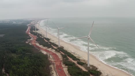 array of onshore horizontal axis wind turbines located on a long beach coastline with high ocean swell on a cloudy day
