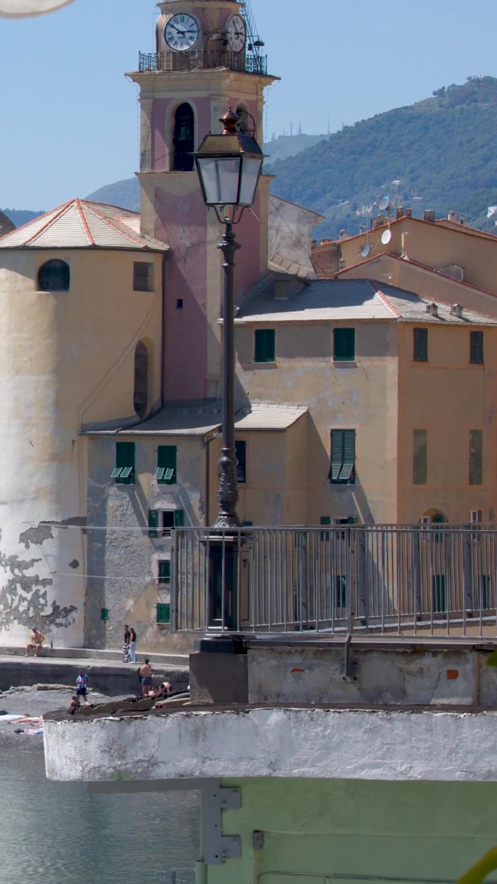 Inquadratura fissa di un campanile mediterraneo e di edifici colorati sotto la luminosa luce solare estiva.