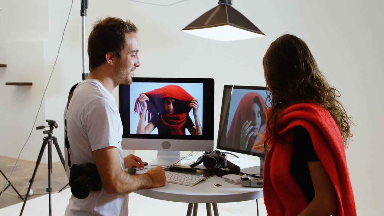 Male photographer showing photos to female model on computer 4k