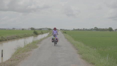 rearview of woman biking through open grassy fields in malaysia with thai flag