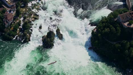4k aerial shot of rhine falls - powerful waterfall with a boat in the current