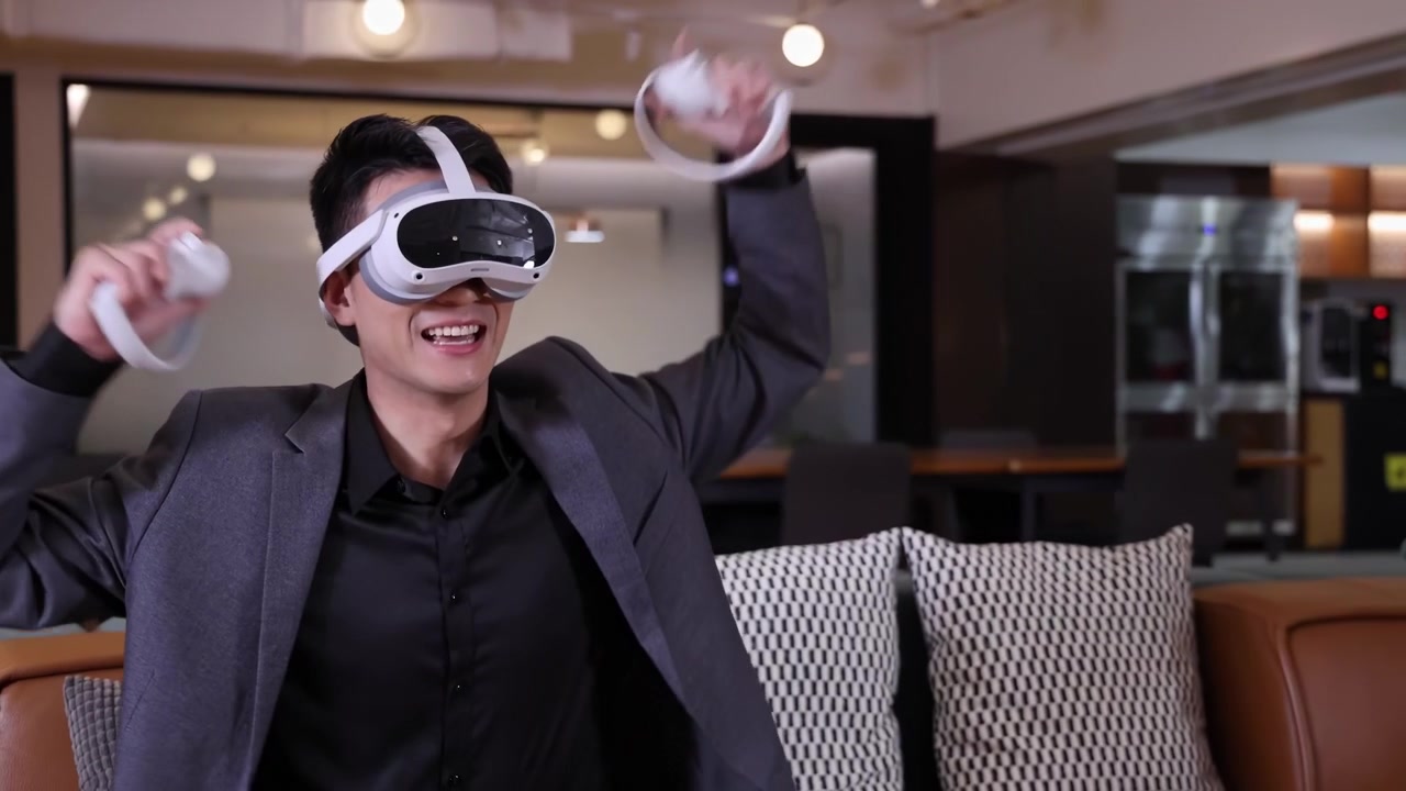 Giovane uomo d'affari in abito che indossa un visore per realtà virtuale 3D (VR) o occhiali per realtà virtuale con tecnologia futuristica e gioca a giochi del metaverso con un telecomando, seduto e che lavora online a un videogioco in sala riunioni