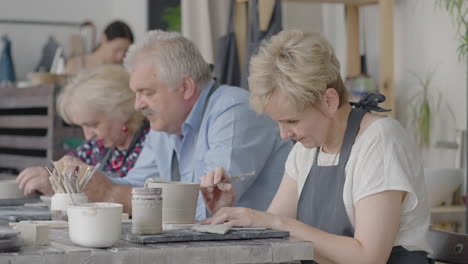 a group of elderly people at a master class in pottery together sculpt and cut a drawing on cups of clay for the manufacture of ceramic dishes