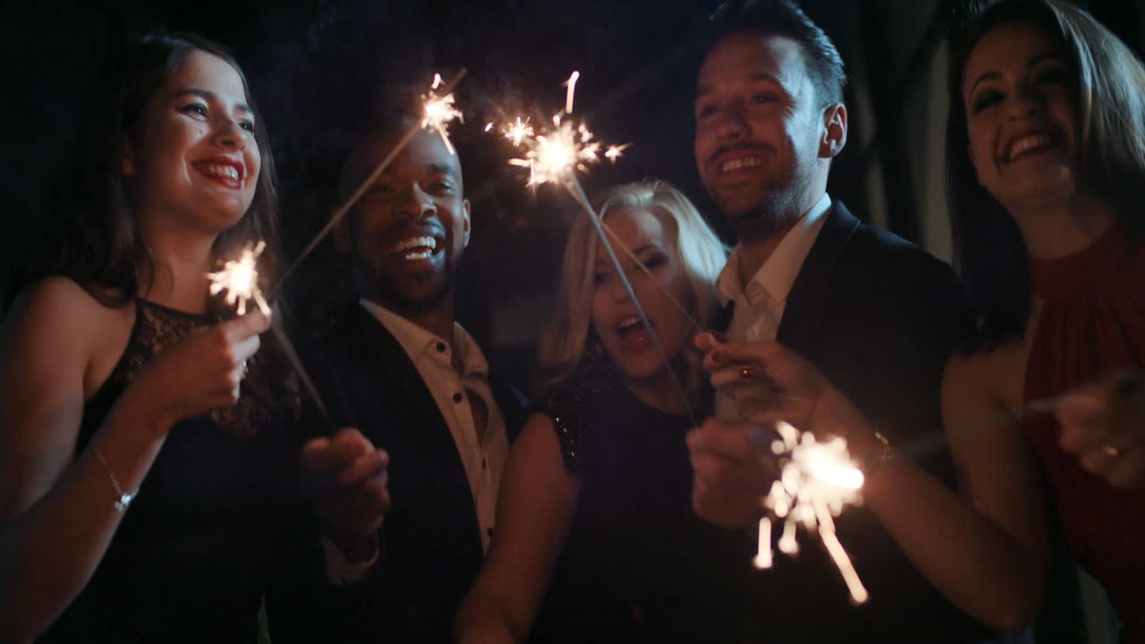 Gruppo di amici affascinanti a una festa glamour che accendono stelle filanti