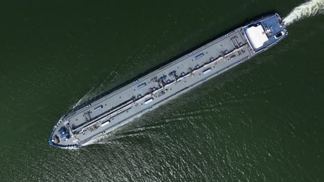 oil tanker ship navigating along waterway, aerial top down view