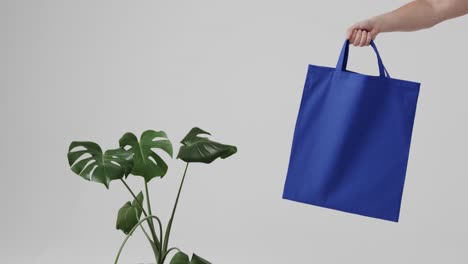 hand of caucasian woman holding blue bag with plant on white background, copy space, slow motion