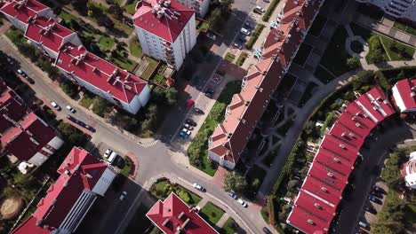 Vista-Aérea-De-Arriba-Hacia-Abajo-Sobrevolando-La-Ciudad-Mostrando-Casas-De-Barrio-Con-Techos-Rojos-También-Autos-Estacionados-Y-Luego-Volando-Sobre-El-Cruce-De-Carreteras-Hacia-Más-Casas-4k