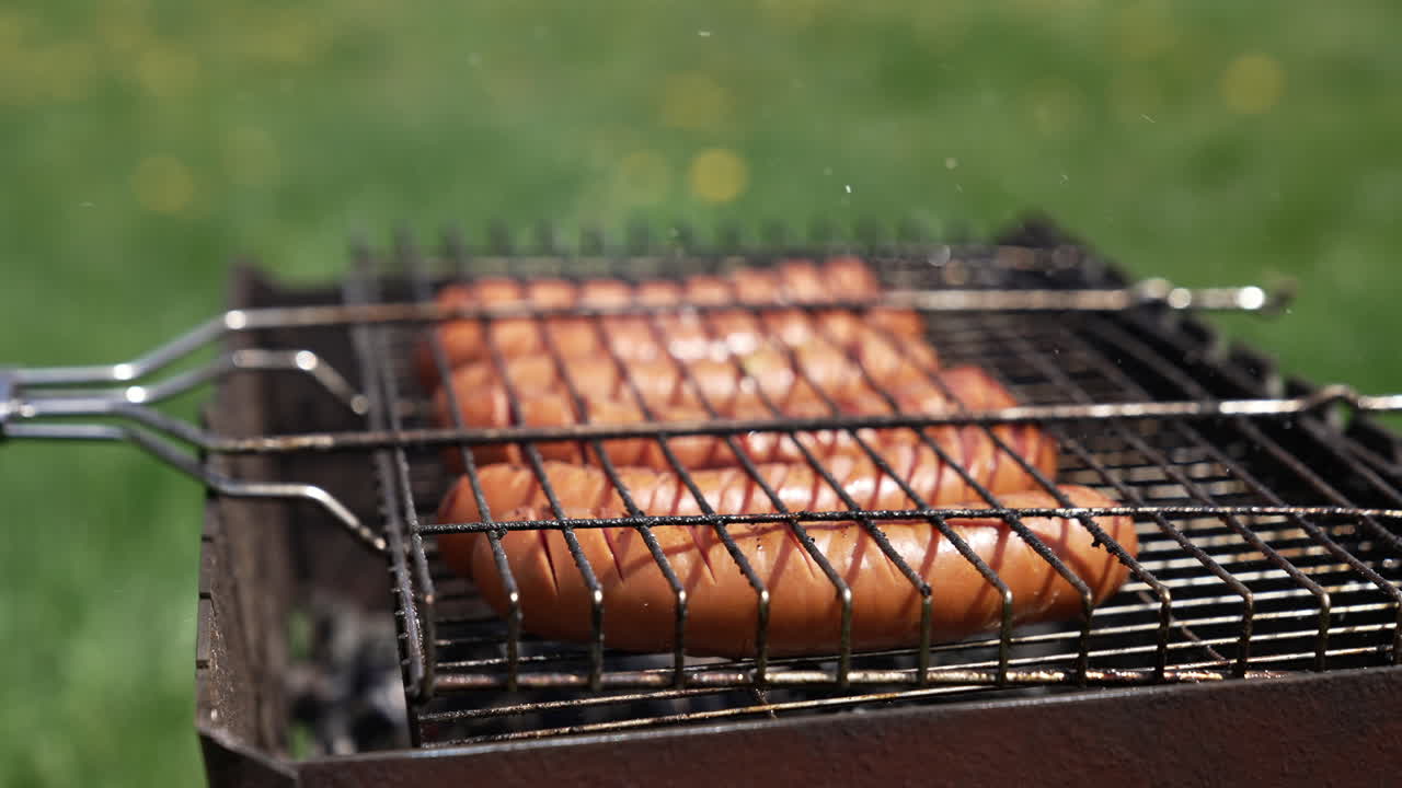 Roasting sausages in smoke. Juicy meat sausages cooking on a grill plate outdoors. Grilling food during summer vacation. Close-up.