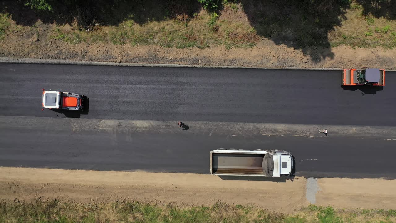 Heavy machinery leveling up new asphalt. Road rollers working on the highway in summer. New road construction. View from above. Motion camera bottom up.
