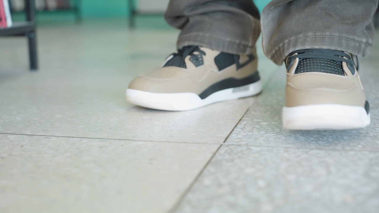 밝은 표정의 젊은 아프리카 남성이 모자를 거꾸로 쓰고 캐주얼한 복장을 입은 채 현대적인 도서관에 서서, 다채로운 책으로 가득 찬 높은 책장에 둘러싸여 한 손에는 닫힌 책을 들고 따뜻하게 미소짓고 있어요.