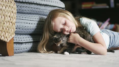 a little girl laying on the floor and petting a kitten as it tries to get away