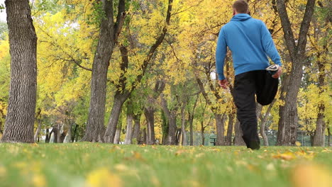 Un-Hombre-Activo-Haciendo-Ejercicios-De-Fitness-En-El-Parque-Con-árboles-Altos-Y-Hierba-Exuberante-Temprano-En-La-Mañana---Toma-A-Nivel-Del-Suelo