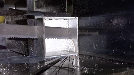 band saw sawing through a aluminum shaped pipe with cooling fluid in super slow motion 800fps