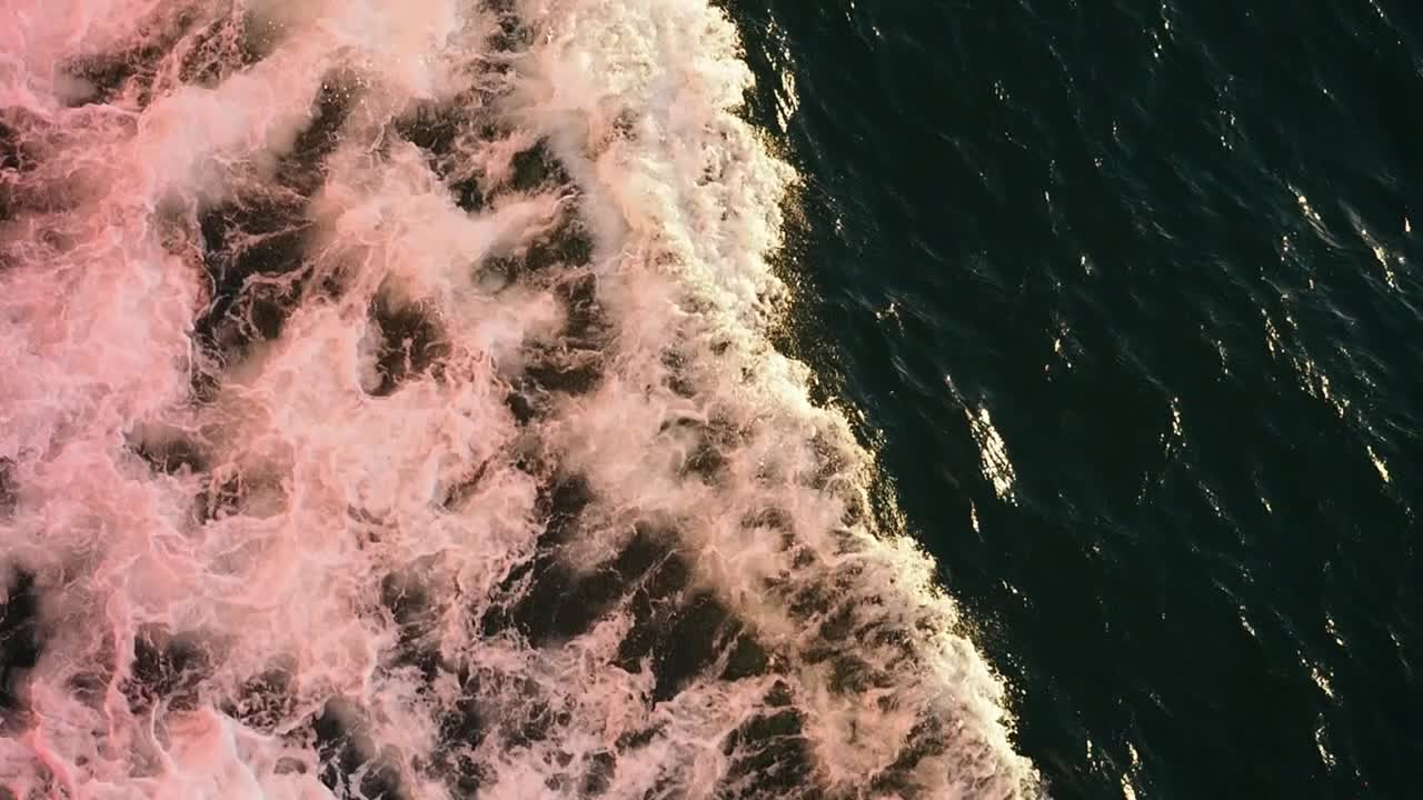 Water rushing around the hull of a ferry, coloured red by the reflected light