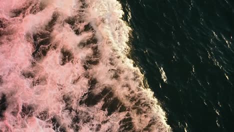 Water-rushing-around-the-hull-of-a-ferry,-coloured-red-by-the-reflected-light