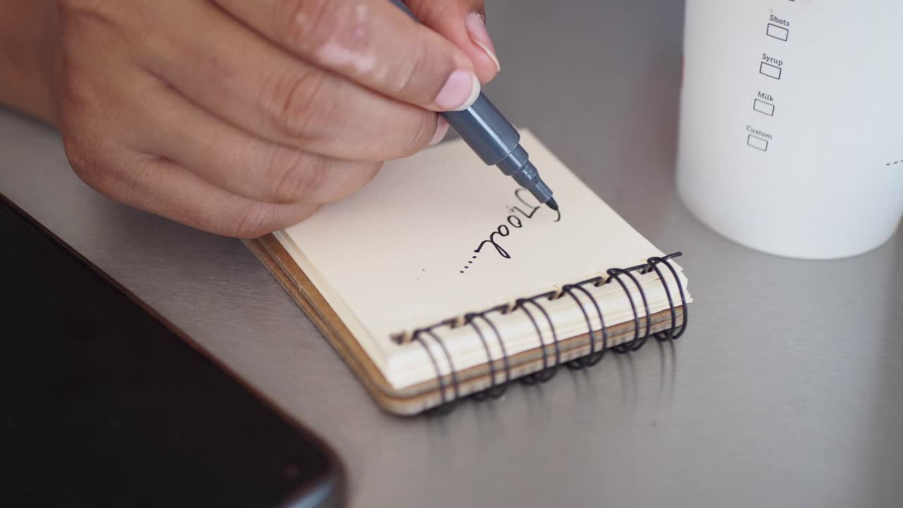 A hand writing on a notepad with a marker, on a table