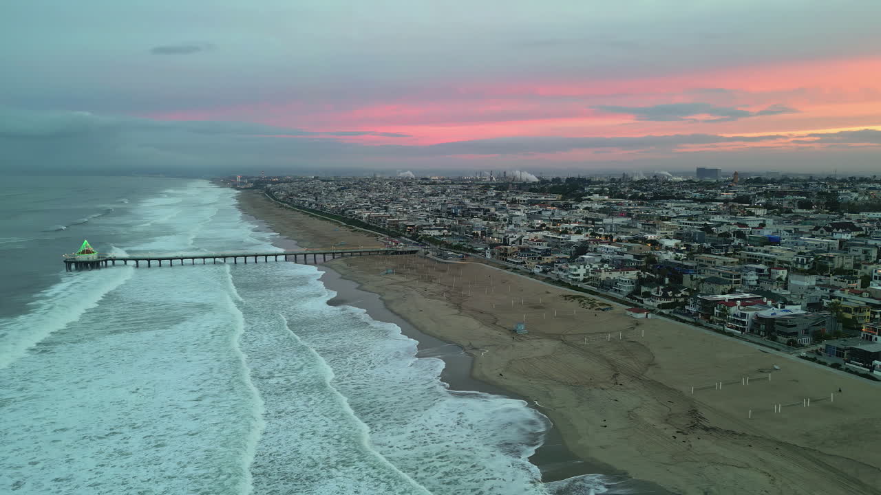 Manhattan Beach Ocean Waves with Pier Overlooking an Urban Cityscape with Morning Pink Sunrise, Aerial Drone Panning Shot
