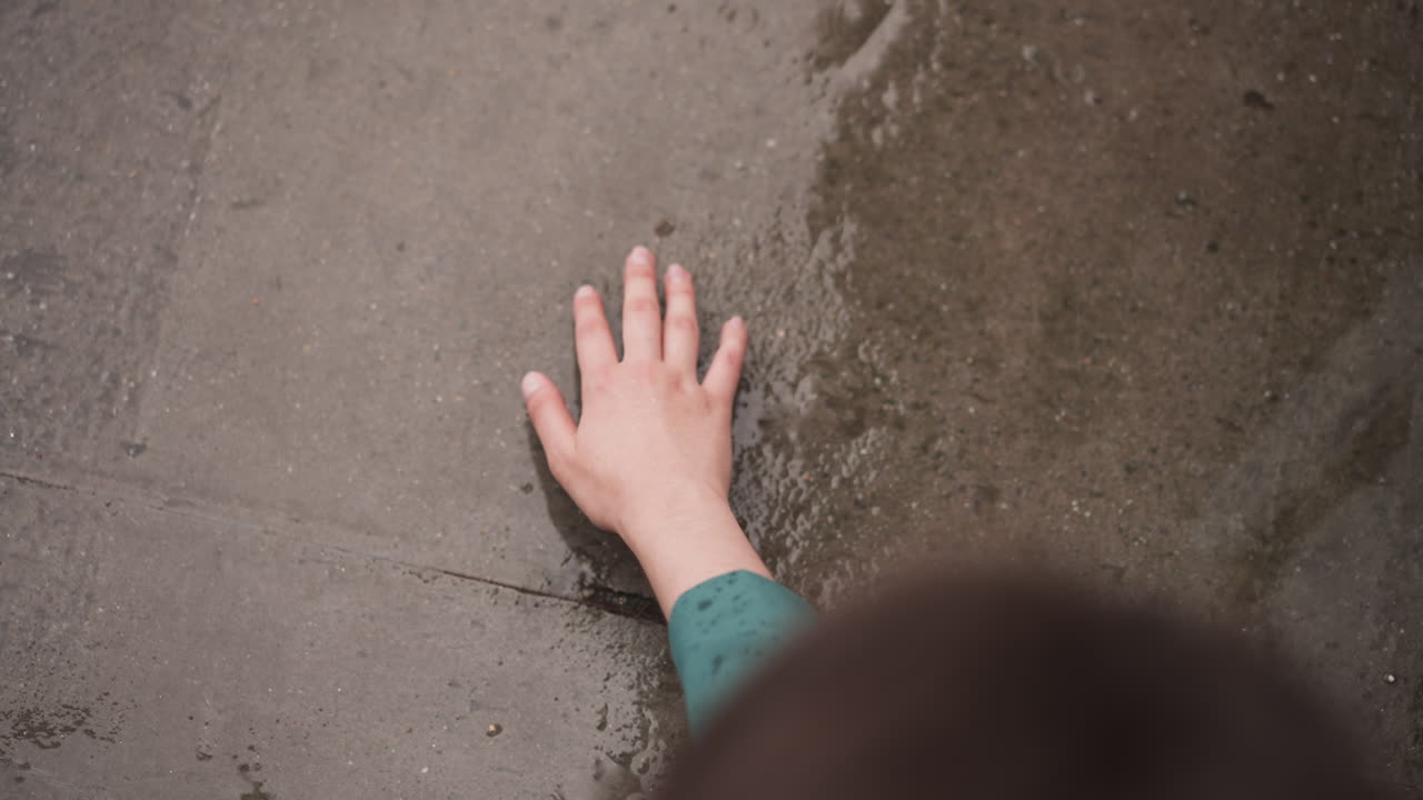la mujer toca el suelo de hormigón húmedo en la lluvia de cerca. la mano de la dama alcanza la superficie de la piedra bajo la gota de lluvia que cae. disfrutando de la frescura en la tormenta de primavera
