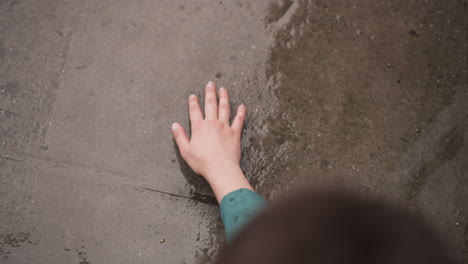 woman touches wet concrete ground at rain closeup. lady hand reaches to stone surface under falling raindrop. enjoying freshness at spring storm