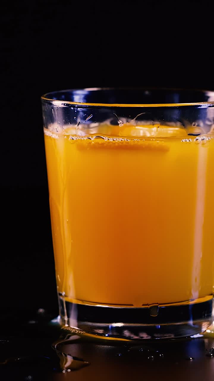 Succo d'arancia vivace schizza all'interno di un bicchiere trasparente su uno sfondo scuro e minimalista.