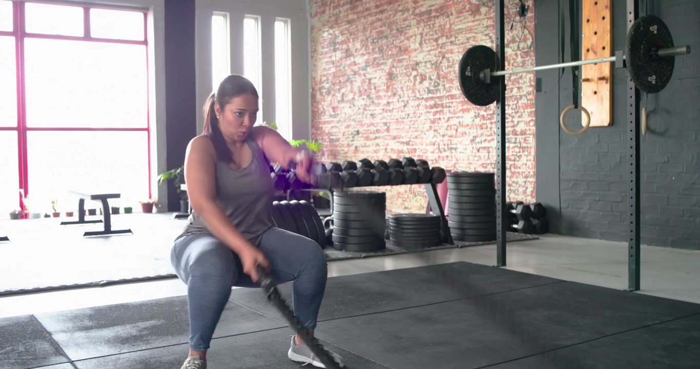 Atleta che afferra le battle ropes ed esegue onde con la corda in squat per aumentare la forza prima di legarsi i capelli.