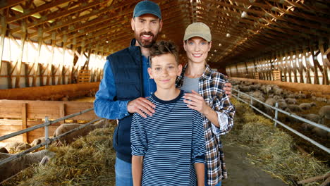 portrait of caucasian happy mother and father with teenage son smiling at camera in stable wih sheep flock