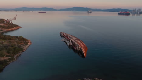 Aerial:-Orbit-shot-of-half-sunken-shipwreck-in-Elefsina,-Greece-during-sunset