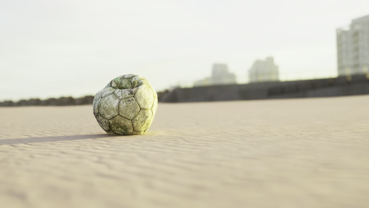 una pelota de fútbol descansa en una playa de arena con edificios de la ciudad en el fondo