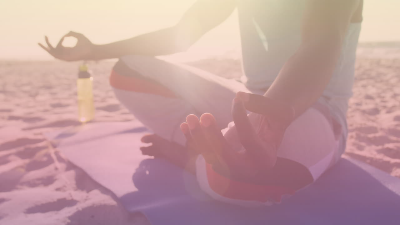 Animation of light spots over african american man meditating at beach