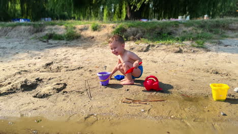 adorable happy toddler playing in the sand on the river bank. smiling child pays with bucket and shovel.
