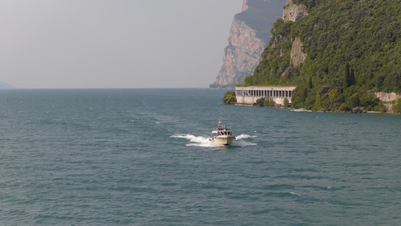 Spettacolari riprese con drone in 4K del Lago di Garda, Italia: un taxi acqueo scivola lungo la riva vicino alla spiaggia, scogliere imponenti e montagne maestose. Catturate in una soleggiata giornata estiva con acqua limpida e un'atmosfera vivace