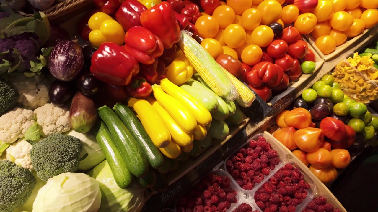 Exposição de produtos sazonais frescos apresentando tomates, abobrinhas, milho, framboesas