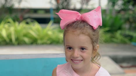 tremendous child with purple bow on head smiles against pool