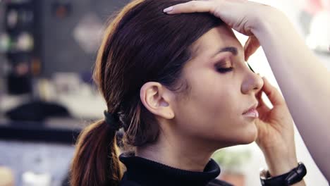 una hermosa chica morena de aspecto caucásico se hace maquillar los ojos por un profesional en un salón de belleza.