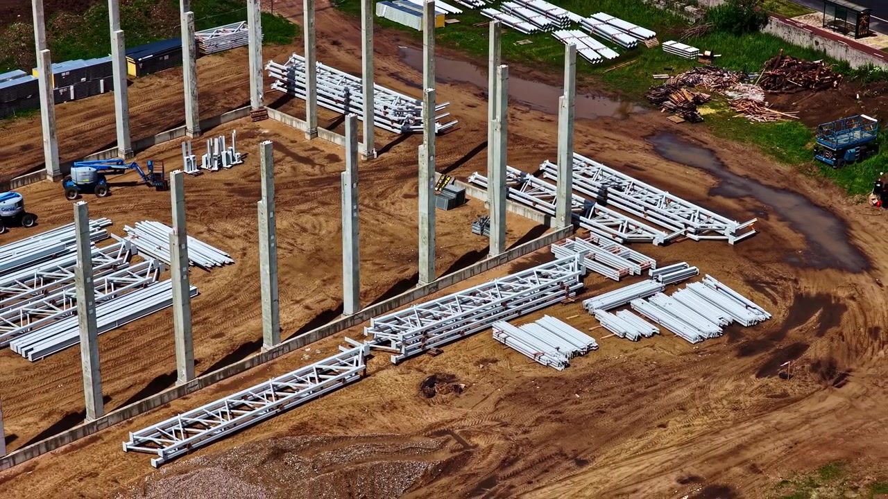 Concrete columns and steel components at industrial warehouse construction site, drone pullback of early stages of small scale data center construction
