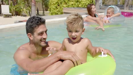 Portrait-of-happy-caucasian-family-playing-with-inflatables-in-swimming-pool