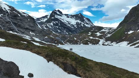 pareja de senderismo en noruega con montañas cubiertas de nieve y un cielo azul claro