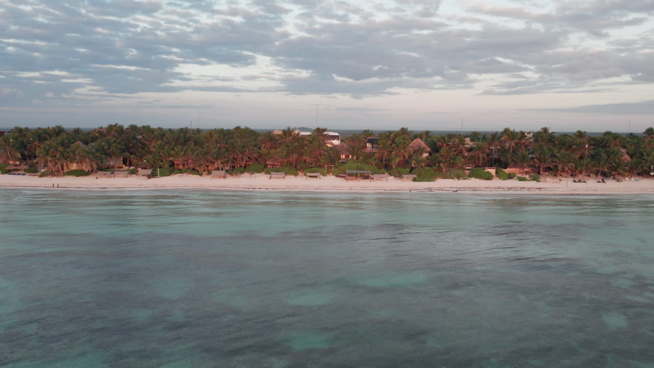 imagen aérea de un océano azul cristalino con playa de arena blanca con palmeras, chozas y cabañas en tulum, méxico