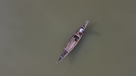 local asian fisherman fishing in dirty river water in small wooden boat, top down