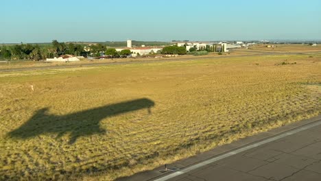 vista lateral izquierda de la sombra de un avión de tamaño medio aterrizando en la pista, temprano en la mañana