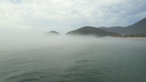 aerial view flying low over the sea and through ocean mist on the coast of brazil