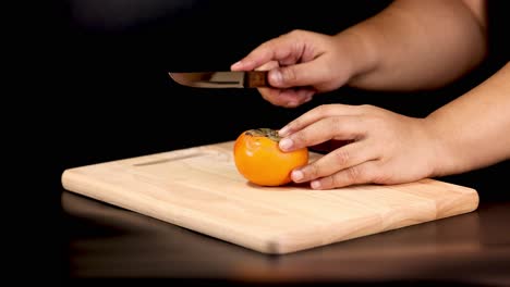 hands slicing persimmon on a wooden board