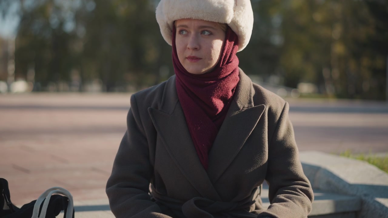 Giovane donna con cappotto invernale e cappello di pelliccia seduta all'aperto.